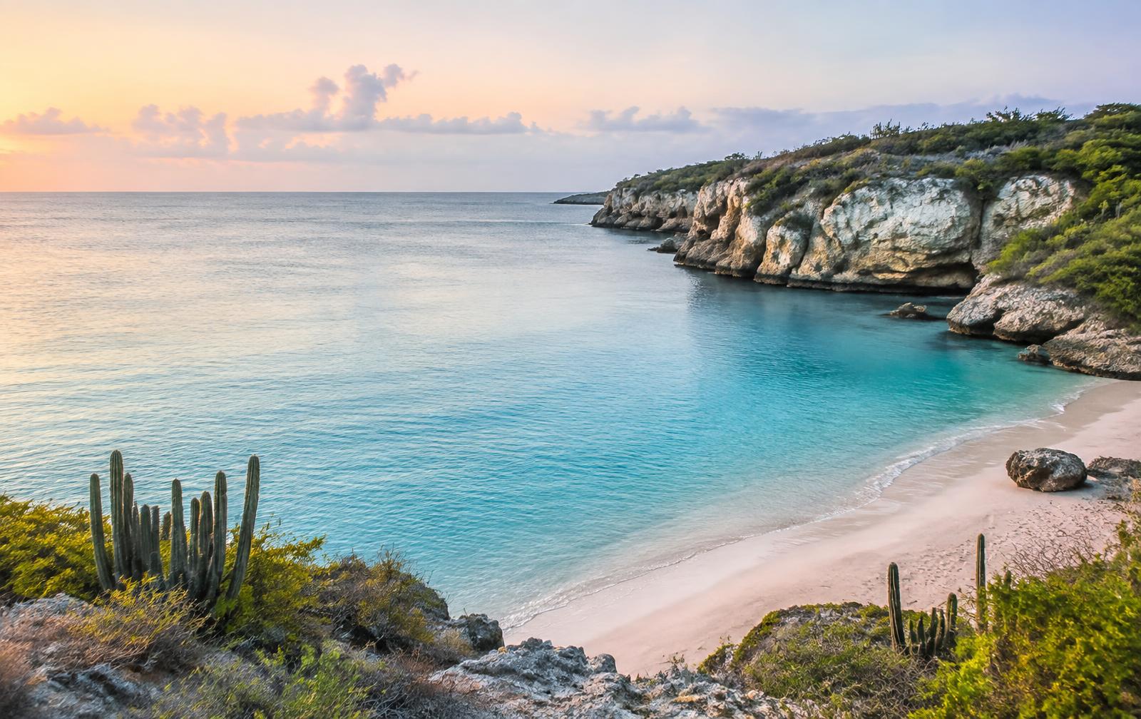 A quiet Curaçao cove beach with turquoise water and limestone cliffs in soft morning light