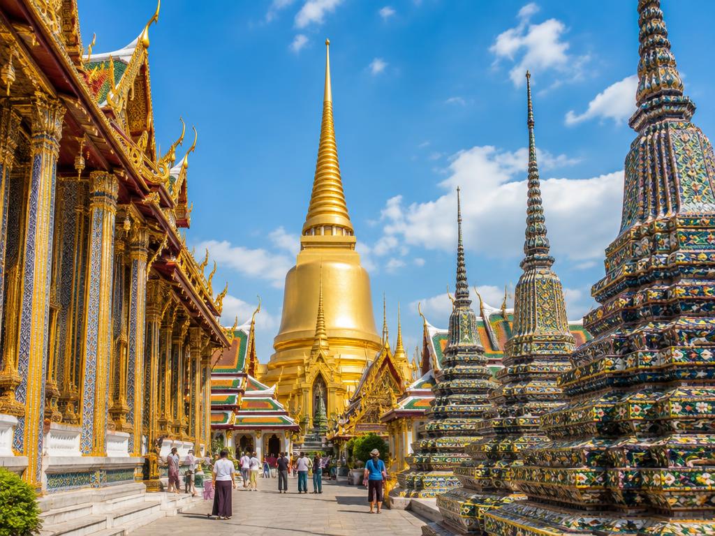 Golden Thai temple spires and mosaic stupas under blue sky